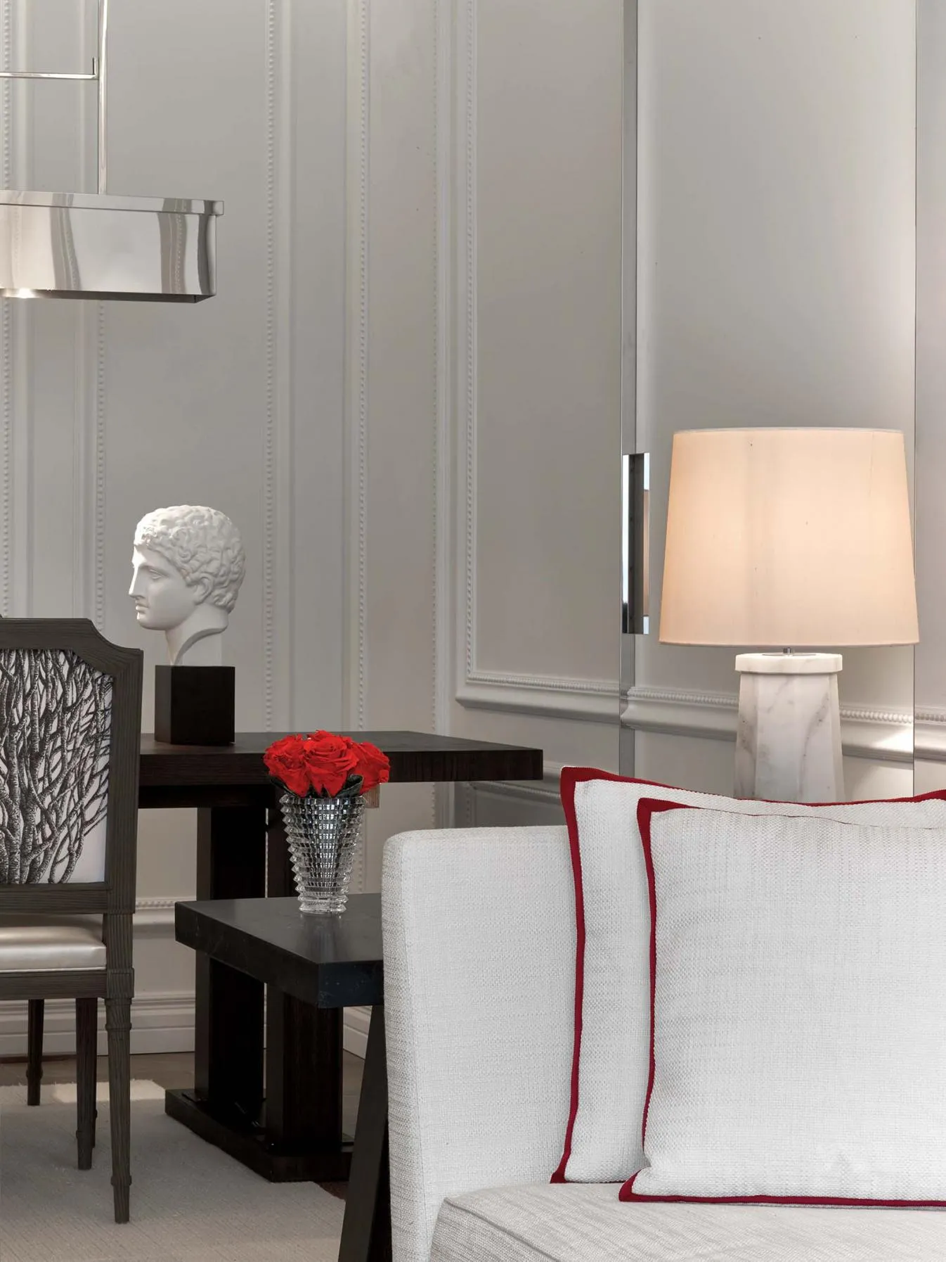 A pale sofa with red-edged cushions, a lamp and decorative bust