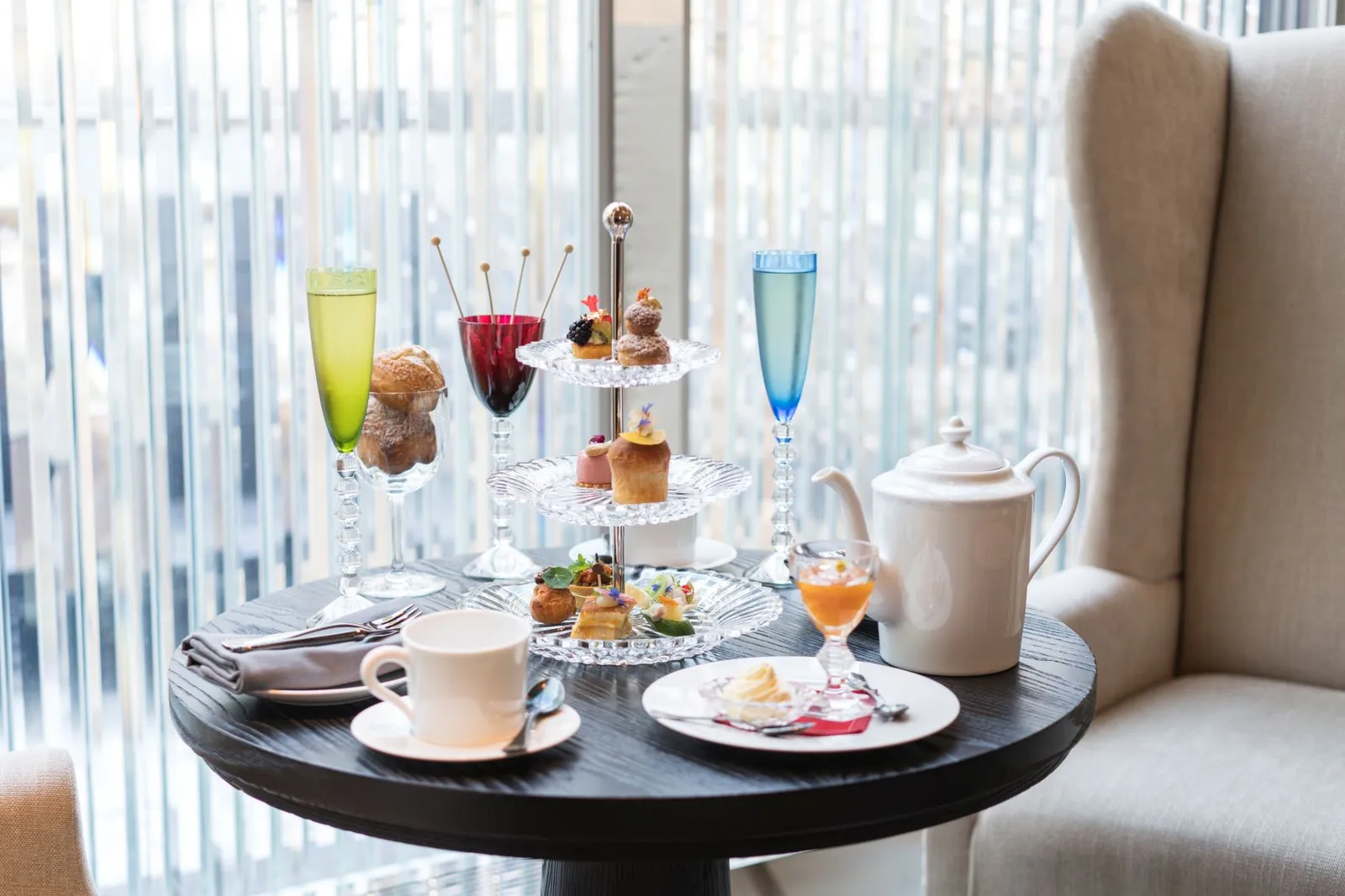 Afternoon Tea featuring baccarat glassware including a 3 tier pastry tower, teapot and saucer set, with various pastries, sweets, and cocktails