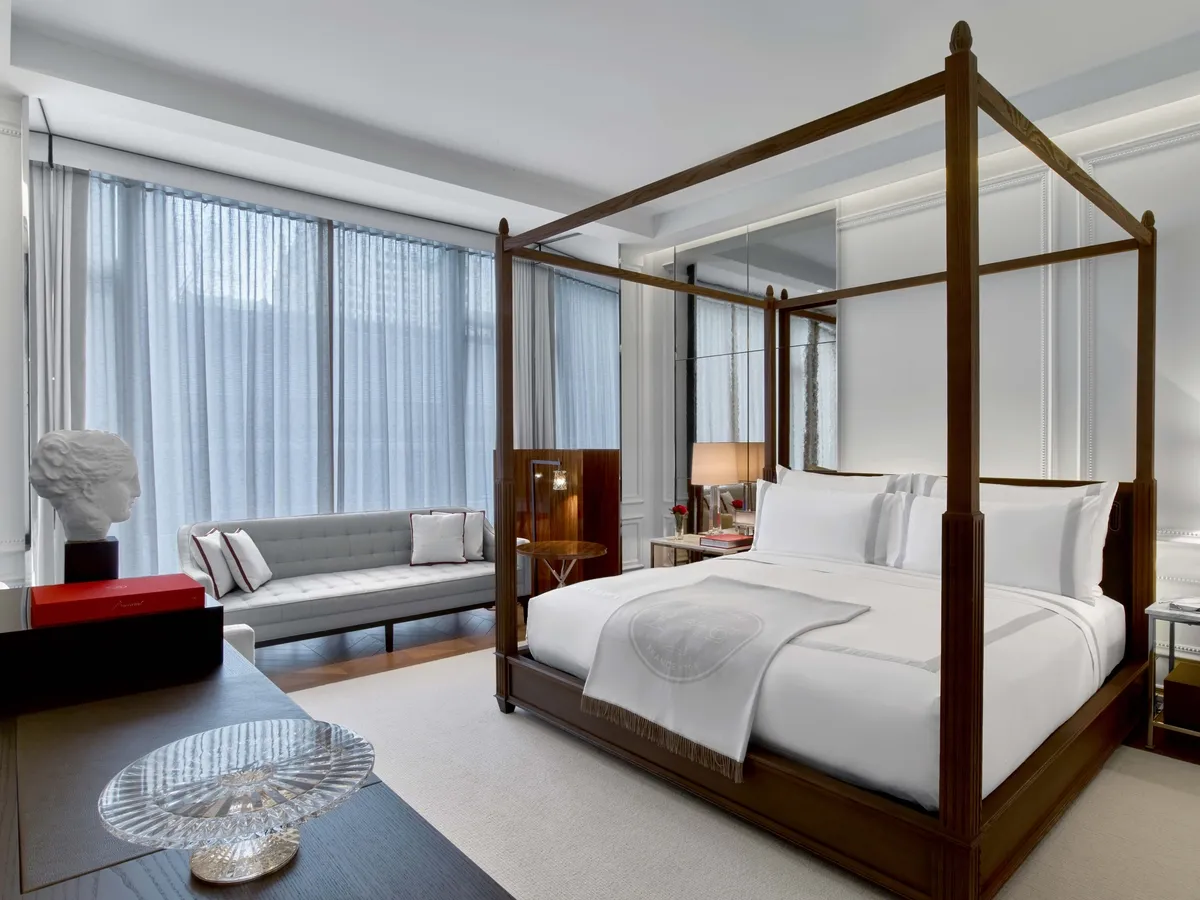 A four-poster bed, pale sofa and desk beside the windows