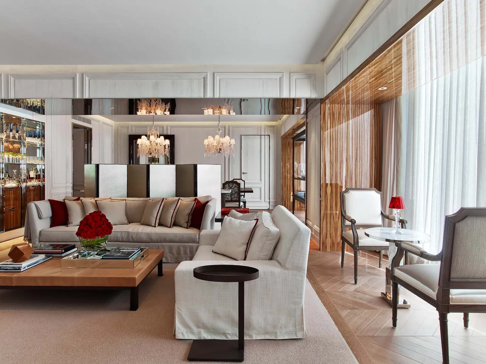 The Baccarat Suite living room with pale sofas, wood panelling and a crystal chandelier