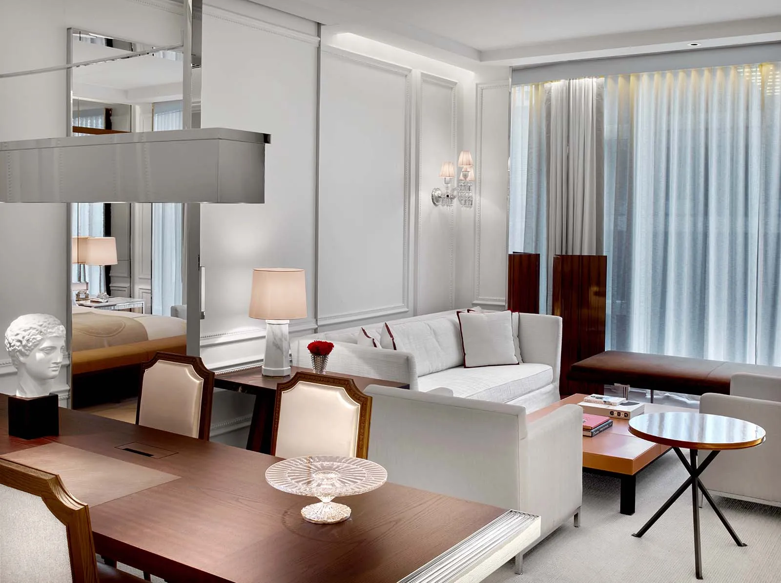 A wooden table, chairs and sofa in a living room, with a bedroom beyond