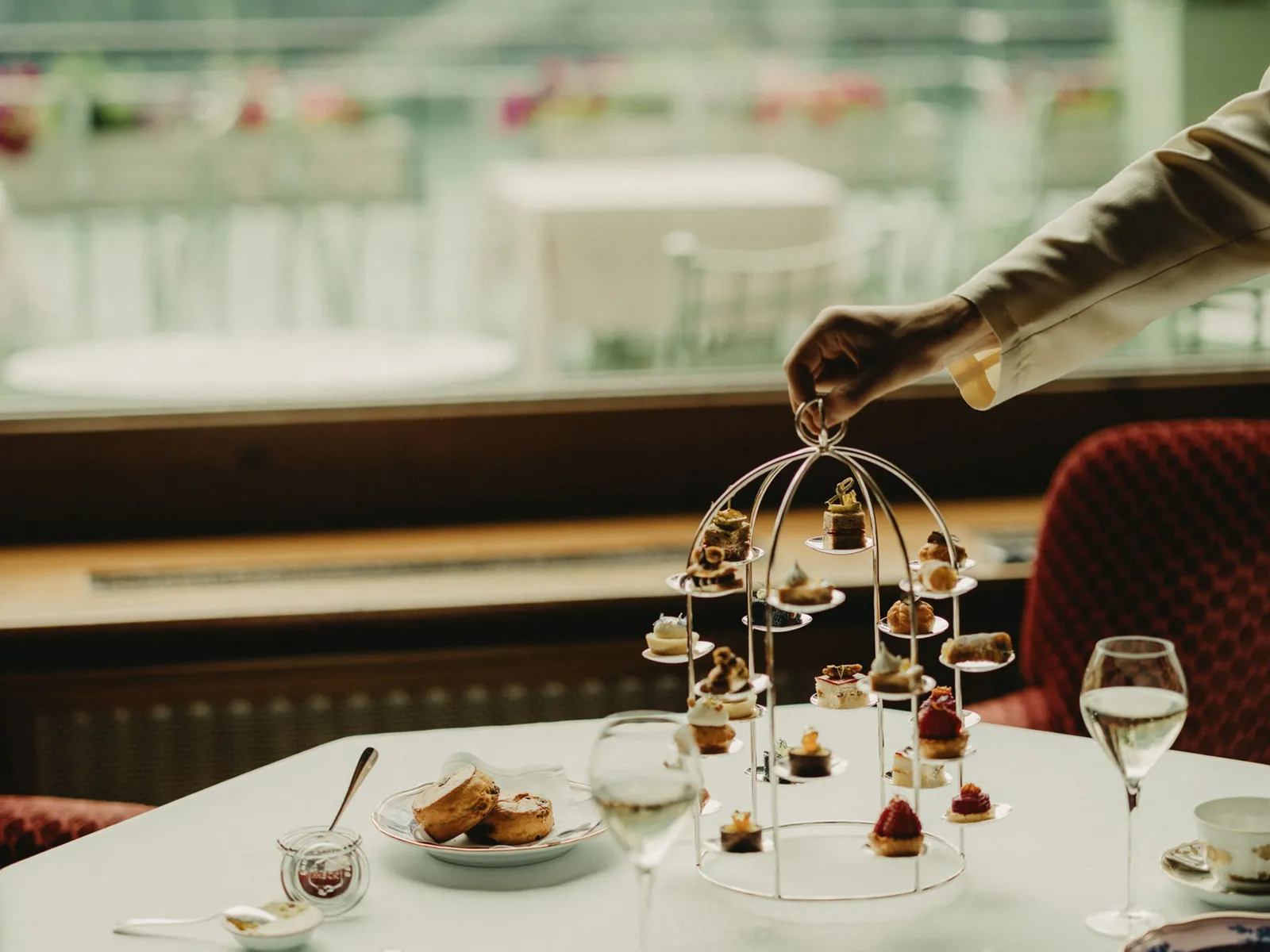 Afternoon tea in Le Grand Hall: a waiter sets down a stand of pastries on a table with scones and 2 glasses.