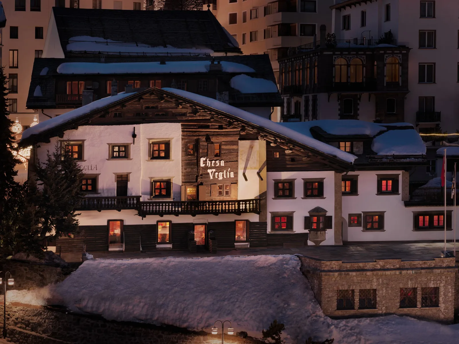 Chesa Veglia on a snowy evening: the white Engadin house with its windows lit and its name painted on the façade.