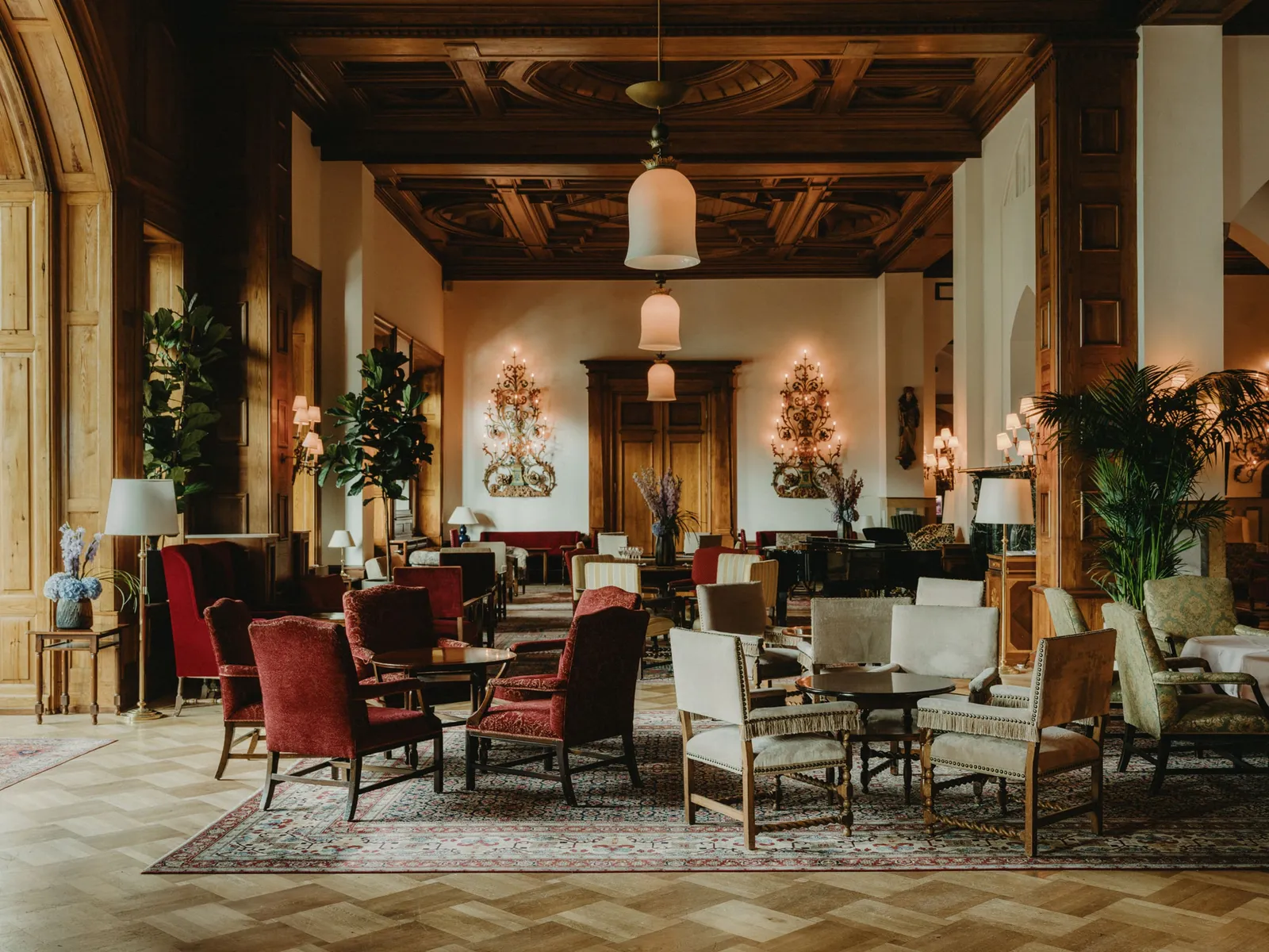 Le Grand Hall: the coffered wooden ceiling, red and pale armchairs on rugs, palms and a lantern hanging in the middle of the room.