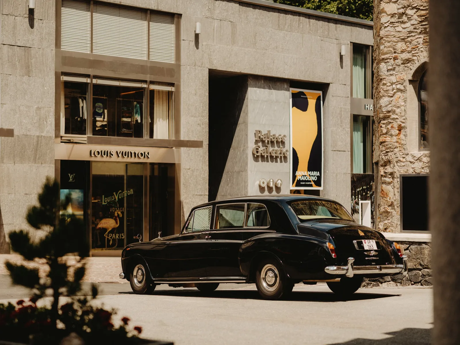 A vintage black Rolls-Royce parked on Via Serlas, in front of the shop windows of the Palace Galerie.