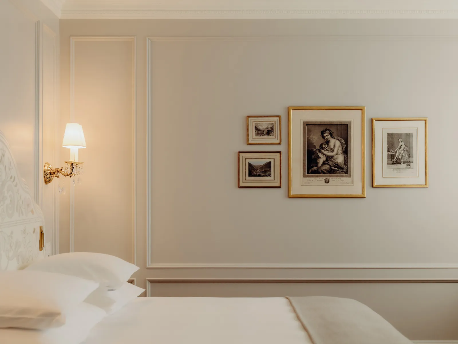 A Deluxe Double Room Village View: the bed, a wall lamp and 3 framed prints on the cream panelled wall.
