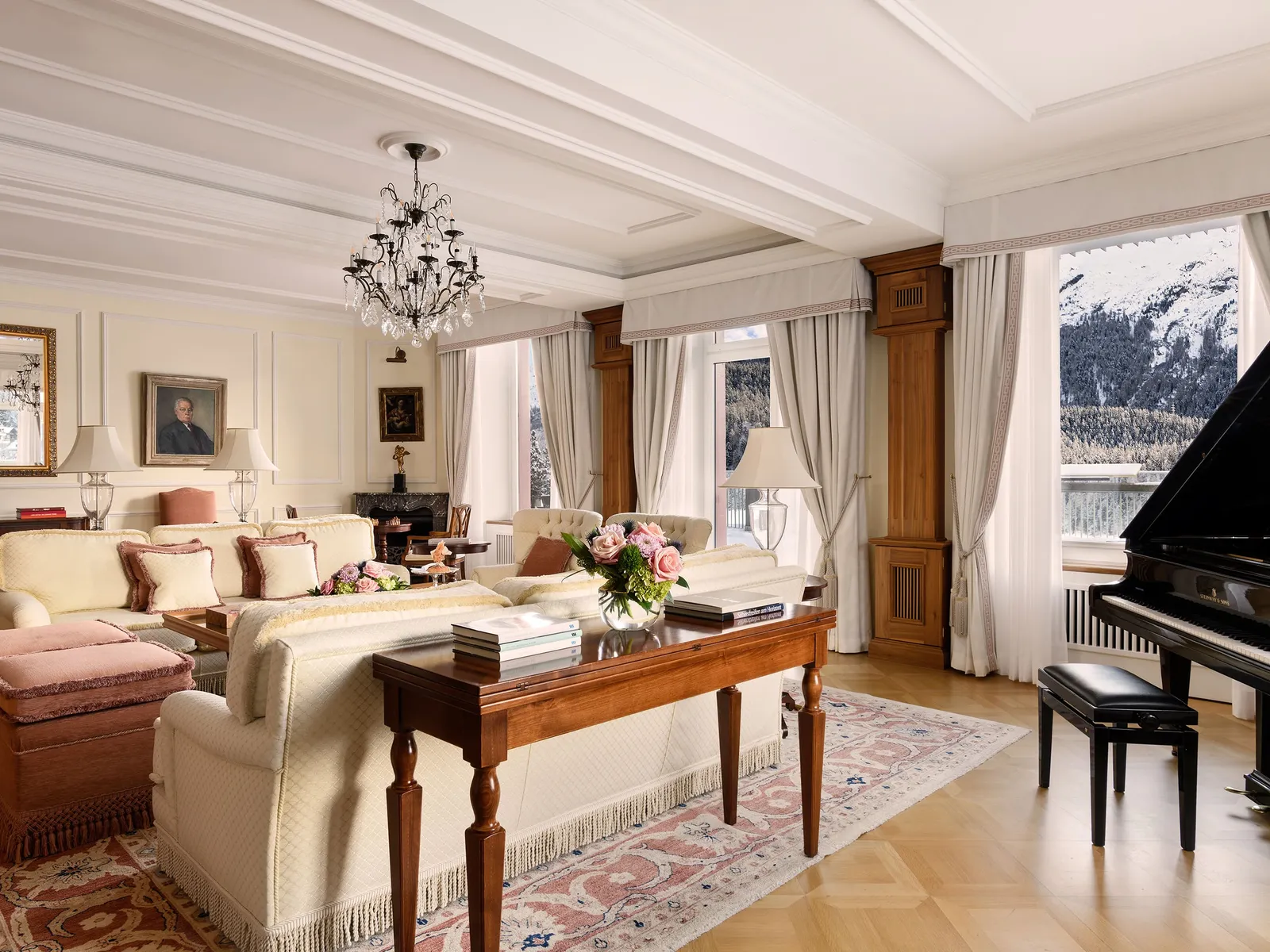 The living room of the Hans Badrutt Suite: the grand piano, pale sofas, a wooden desk and the windows onto the mountains.