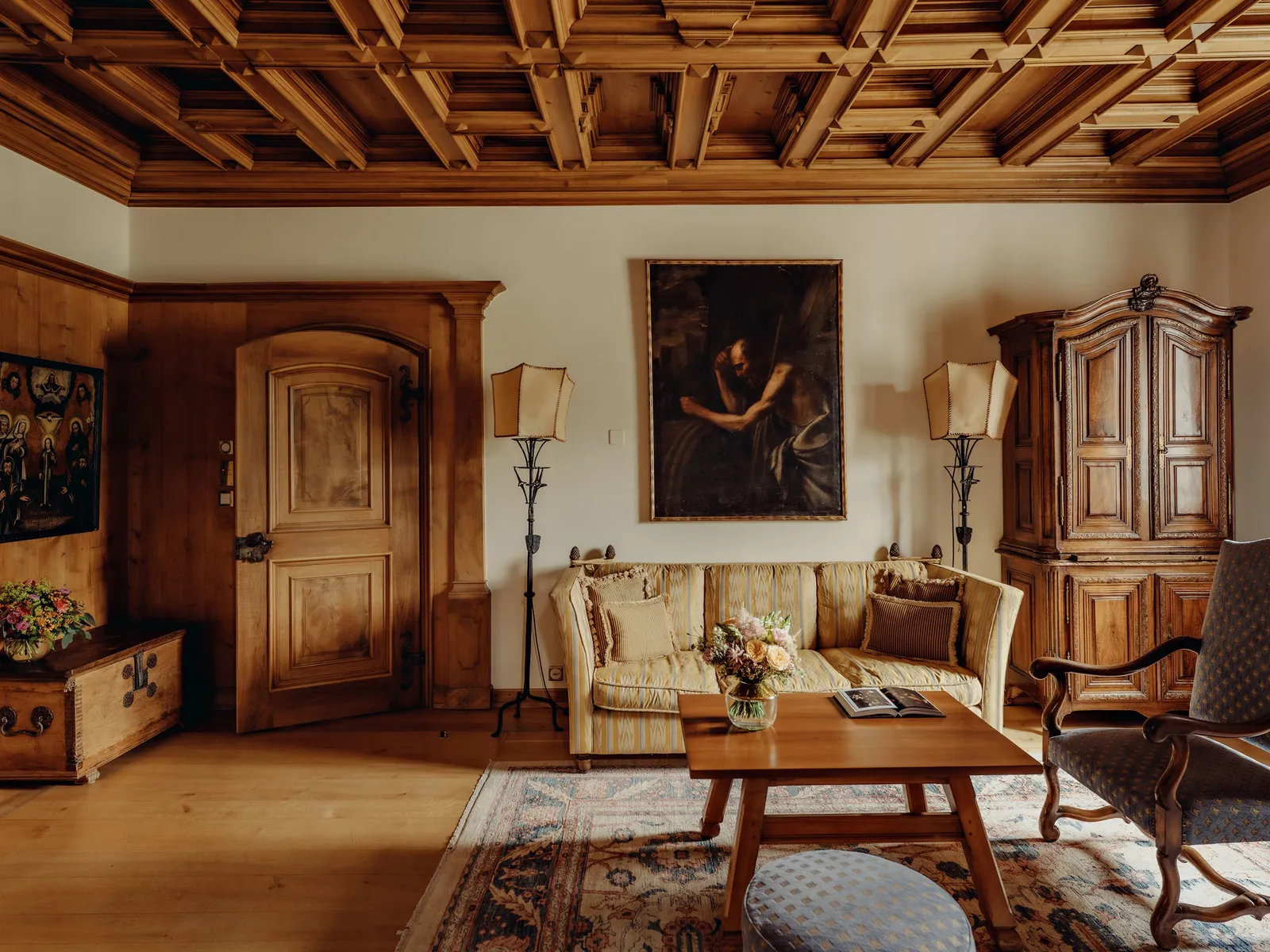 The Hitchcock Suite: the coffered wooden ceiling, a carved wooden door and wardrobe, an old painting and sofas around the table.