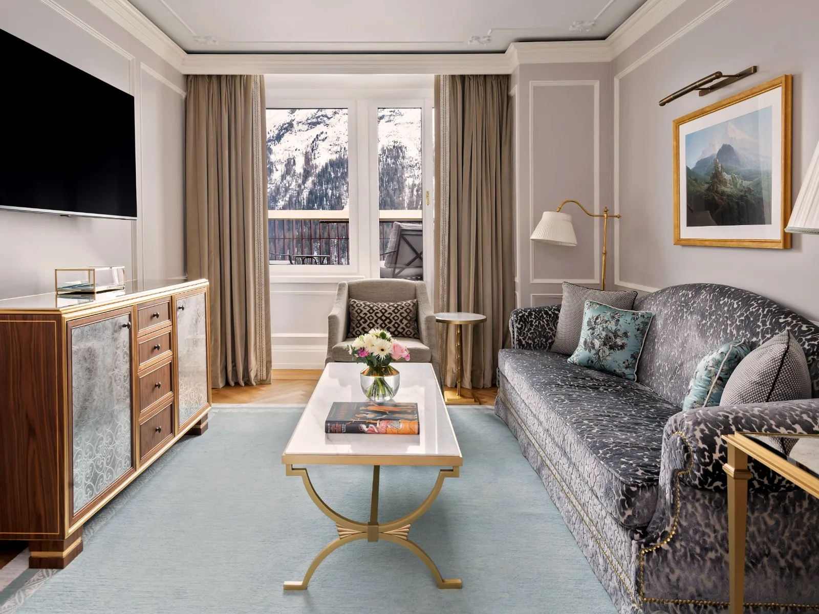 The living room of a Palace Suite: the grey sofa, the marble coffee table, the blue rug and the windows onto the mountains.