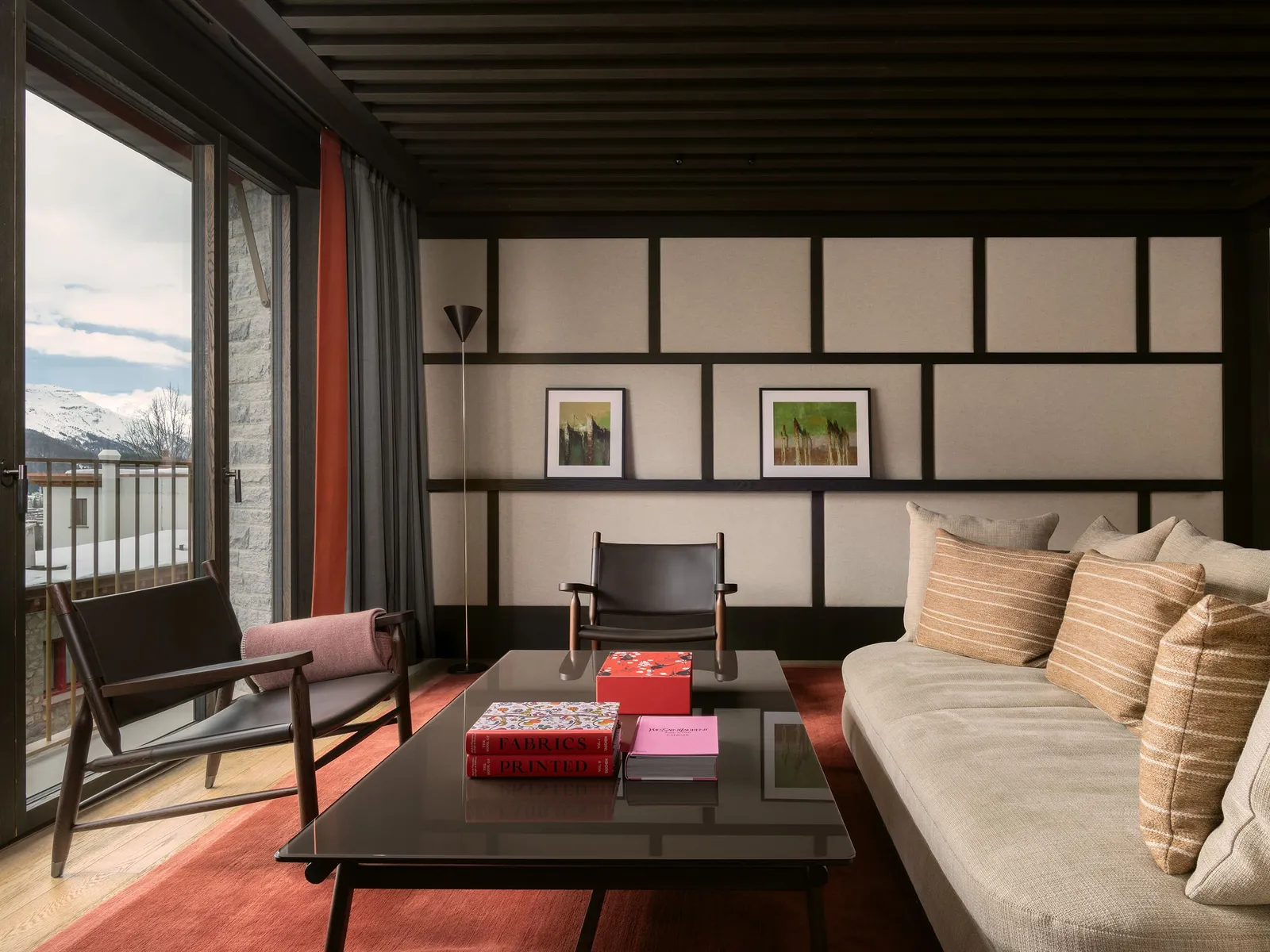 The living room of the Serlas Prestige Suite: the pale sofa with striped cushions, a leather armchair, the black table and the window onto the mountains.