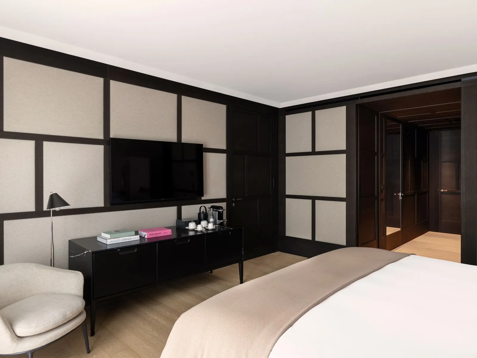 A Serlas Room: pale fabric wall panels with dark frames, the television over the black console and the bed in the foreground.