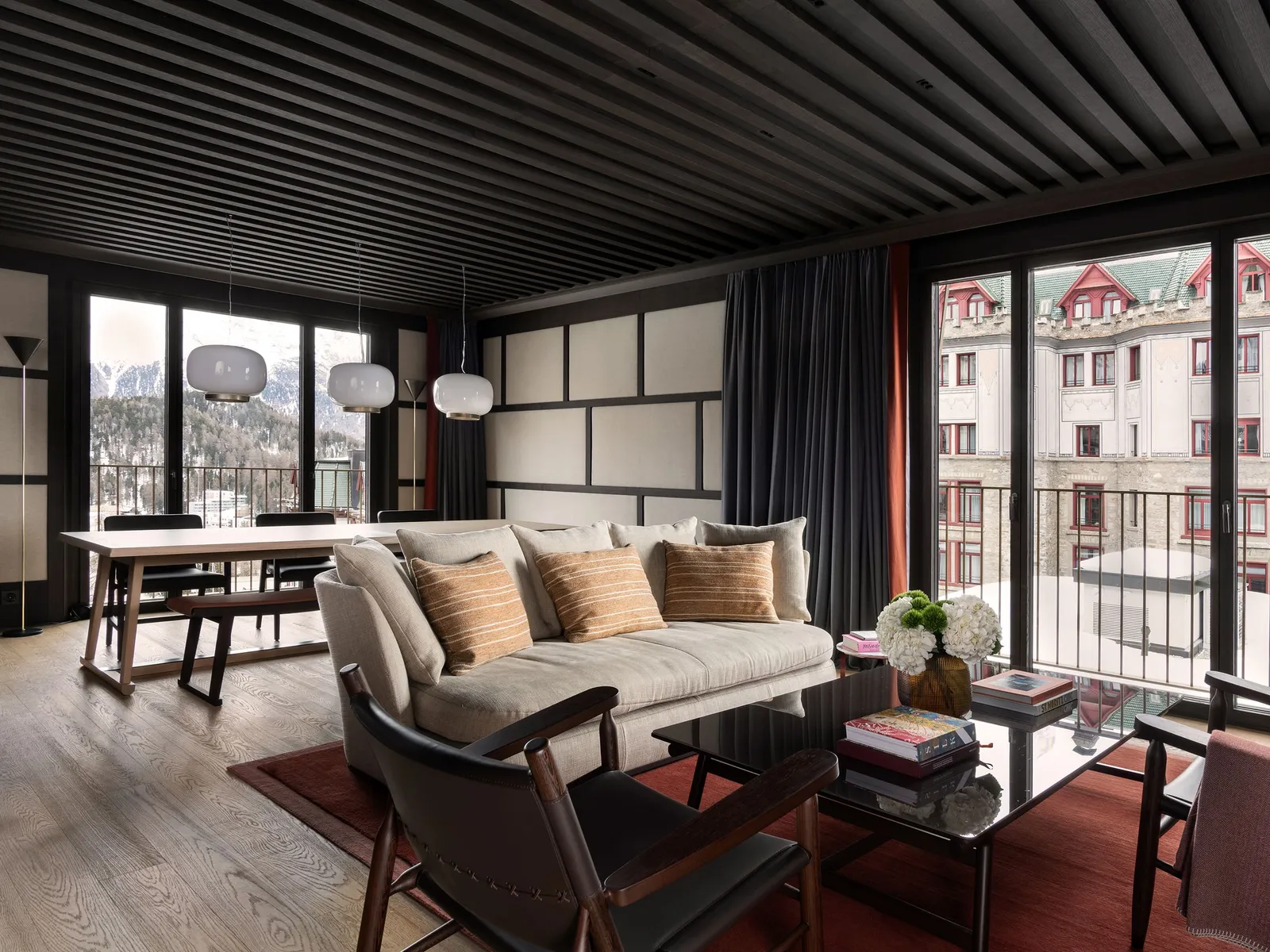 The living room of the Serlas Two-Bedroom Suite: the dining table under glass pendant lamps, the sofa with ochre cushions and windows onto the village.