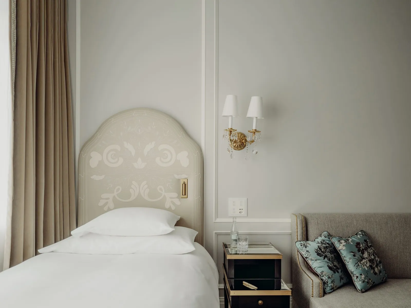 A Superior Single Room: the single bed with its pale carved headboard, a gilt wall lamp and an armchair with blue cushions.
