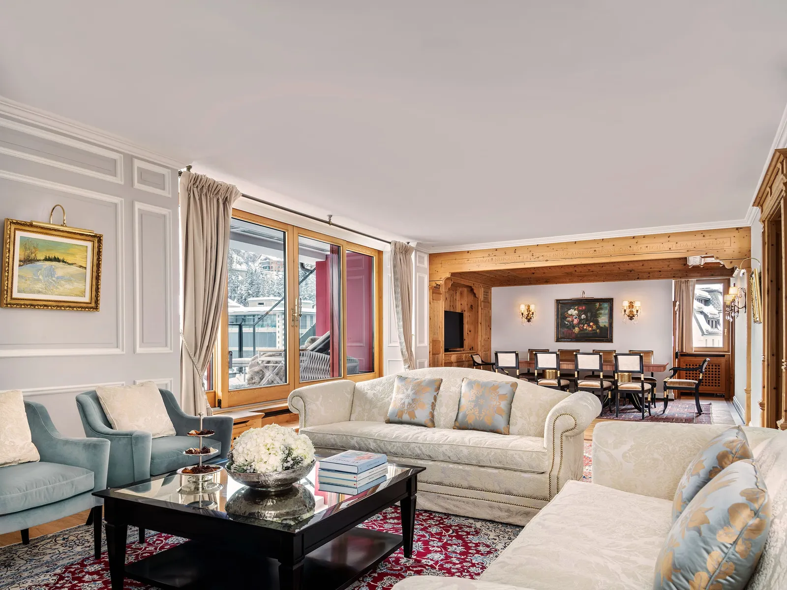 The living room of the Tower Penthouse Apartment: pale sofas around a black table, the dining room beyond and windows onto the village.