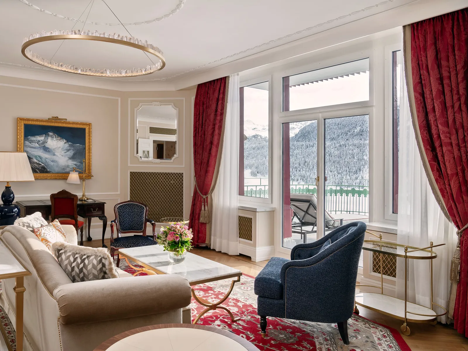 The living room of the Two-Bedroom St. Moritz Suite: pale sofas, a blue armchair, red curtains and French windows to the balcony.