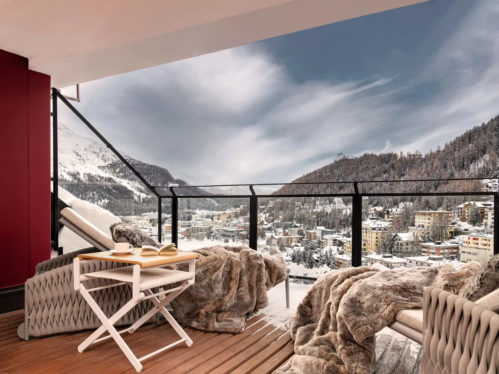 A balcony of the Tower Penthouse Apartment: 2 loungers with fur throws and, below, the snowy roofs of St. Moritz and the forest.