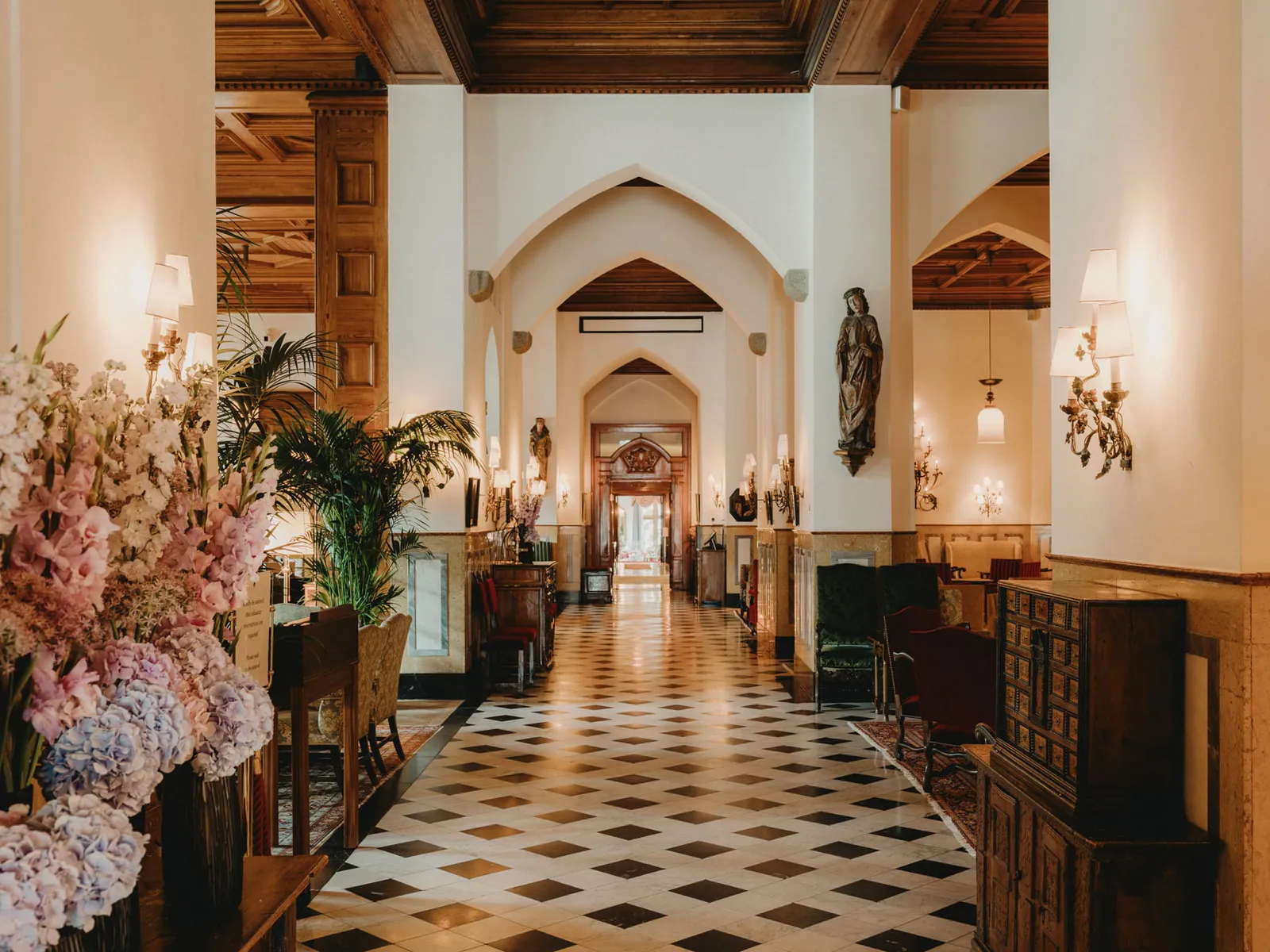 The gallery of Le Grand Hall: the black-and-white chequered floor, pointed arches, a statue on the wall and a large vase of flowers.