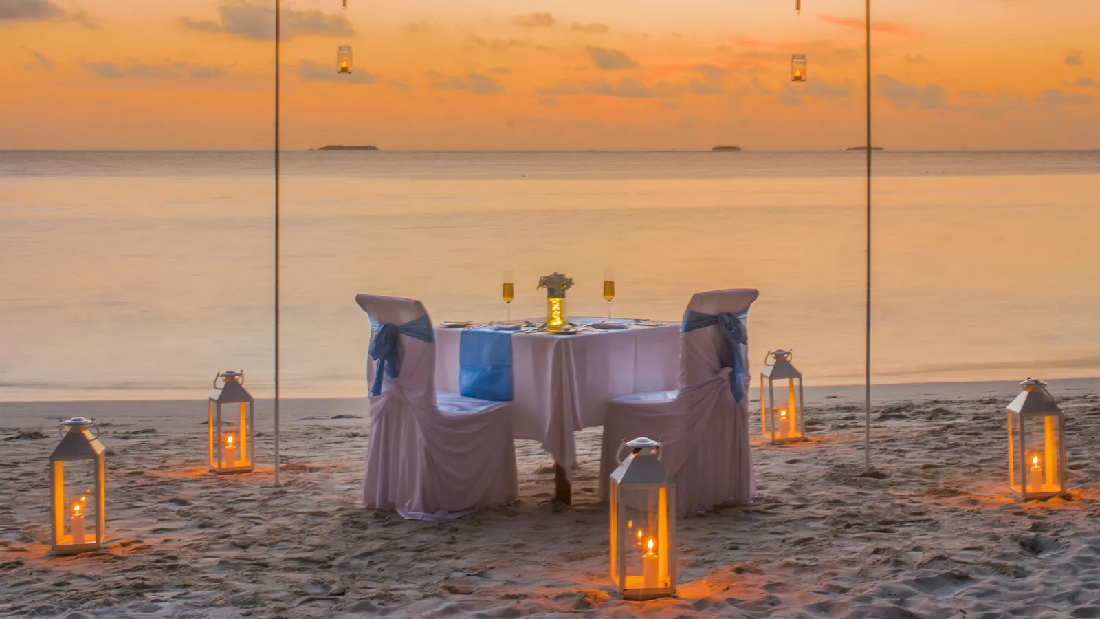 A table for 2 on the sand at sunset, among lanterns