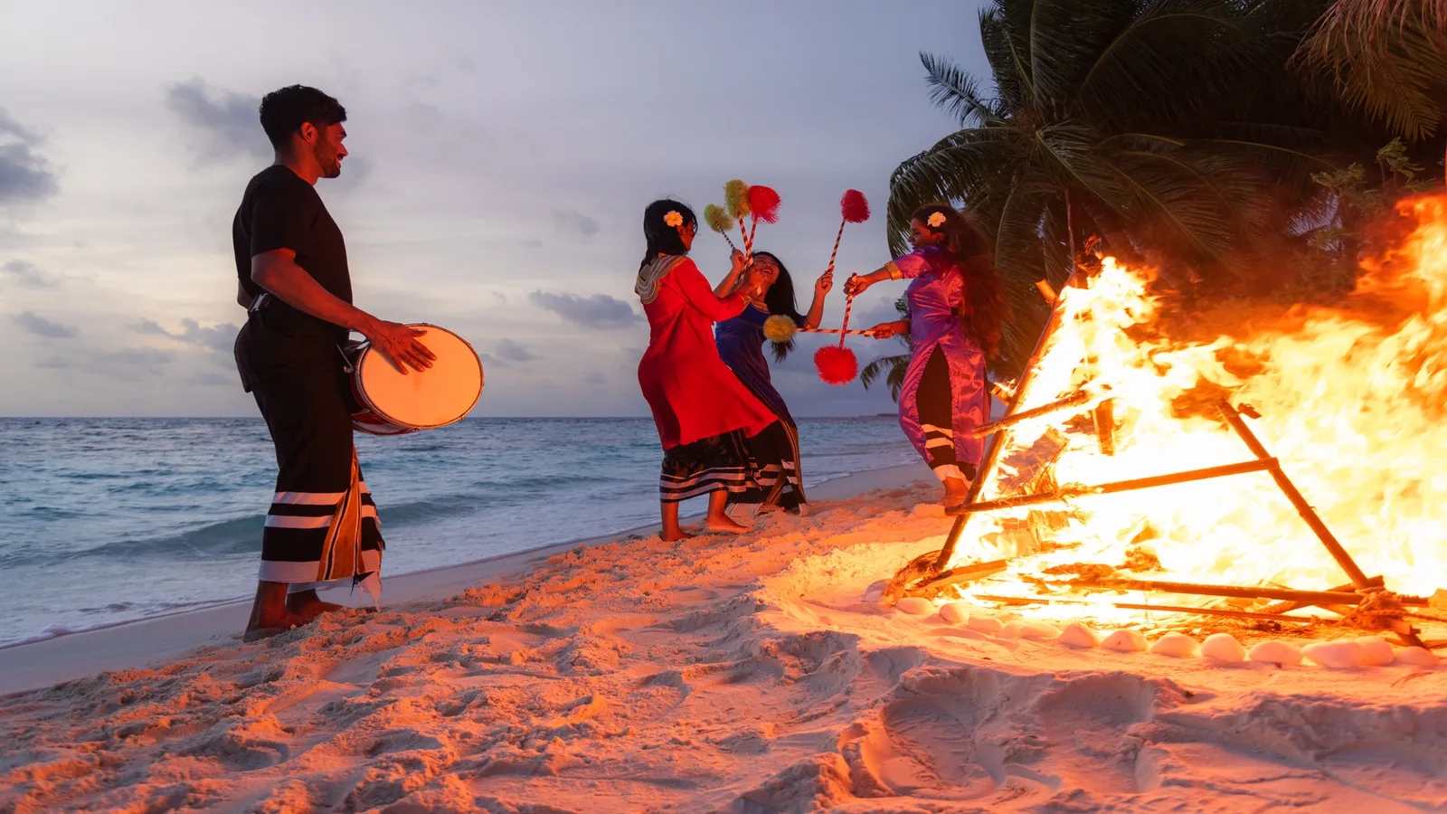 A bodu beru drummer and 3 dancers beside a bonfire on the beach