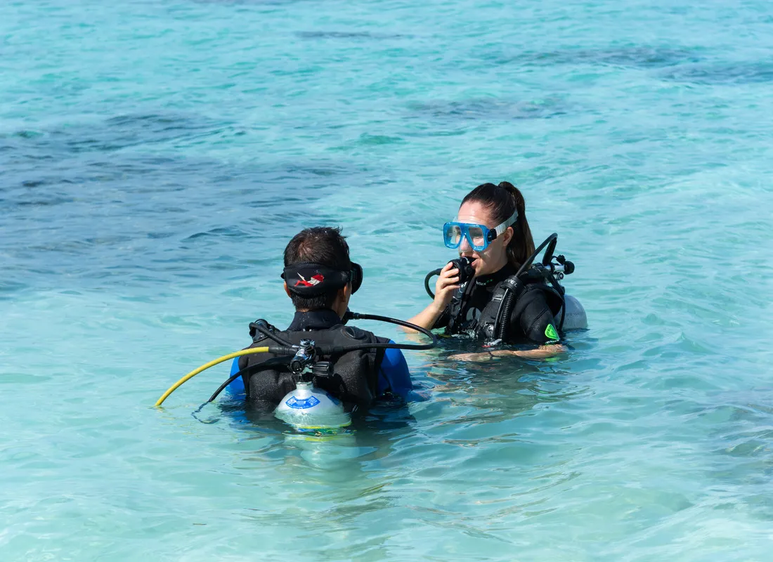 An instructor and a pupil with tanks in the shallow lagoon