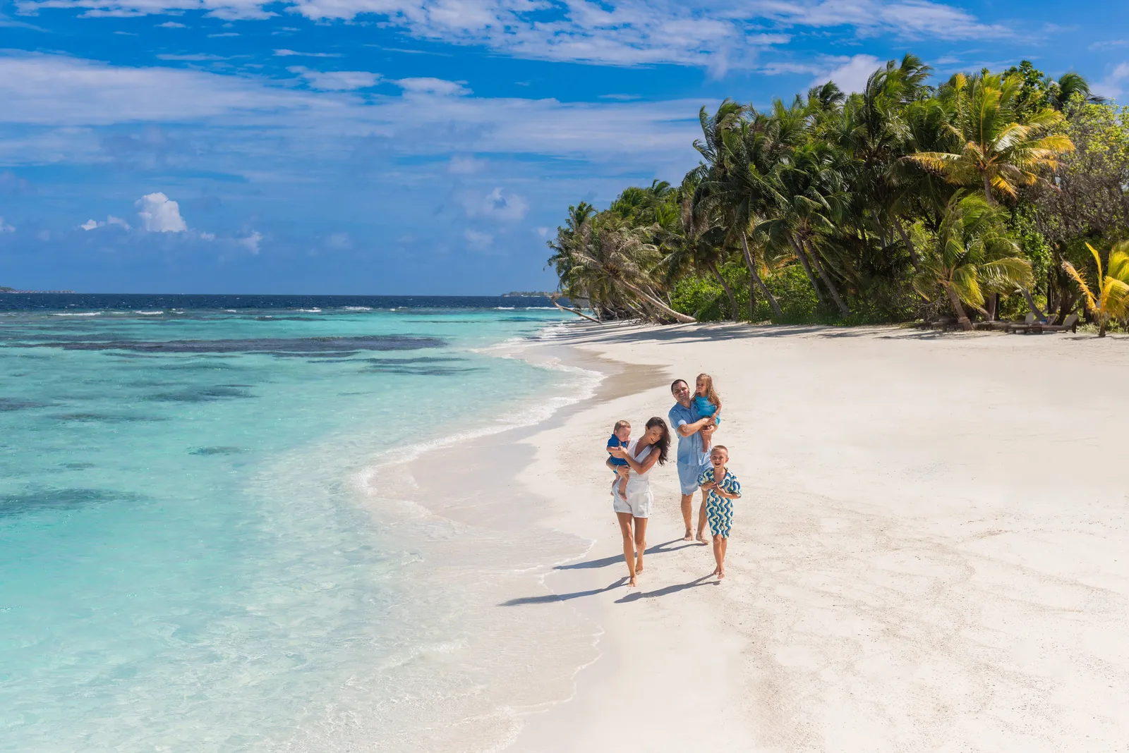 A family with 3 children walking along the shore, between the lagoon and the palms