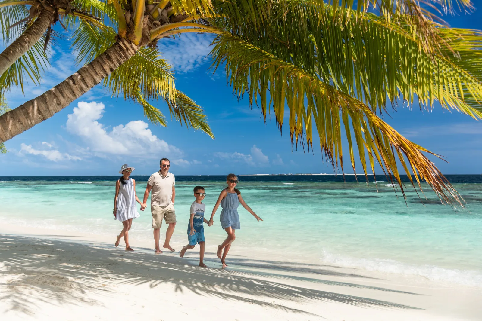 A family running hand in hand along the beach beneath palm fronds