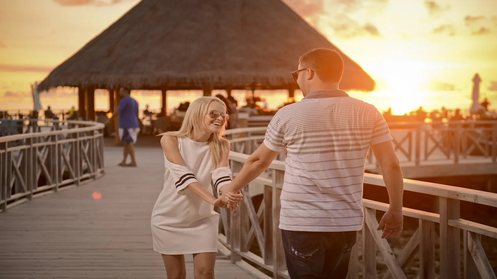 A couple on Huvan’s deck at sunset, beneath the thatched roof