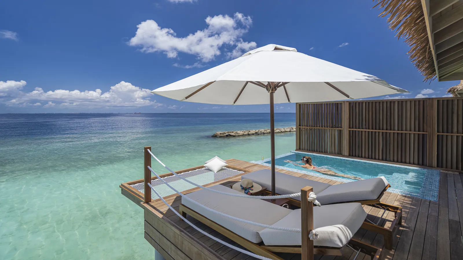 A Sunset Water Villa deck, its loungers, parasol and pool over the lagoon