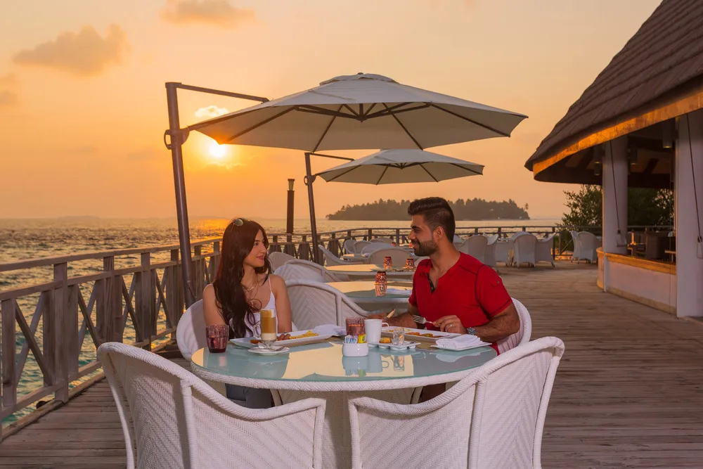 A couple at table on Sea Breeze’s terrace, the sun setting over the sea