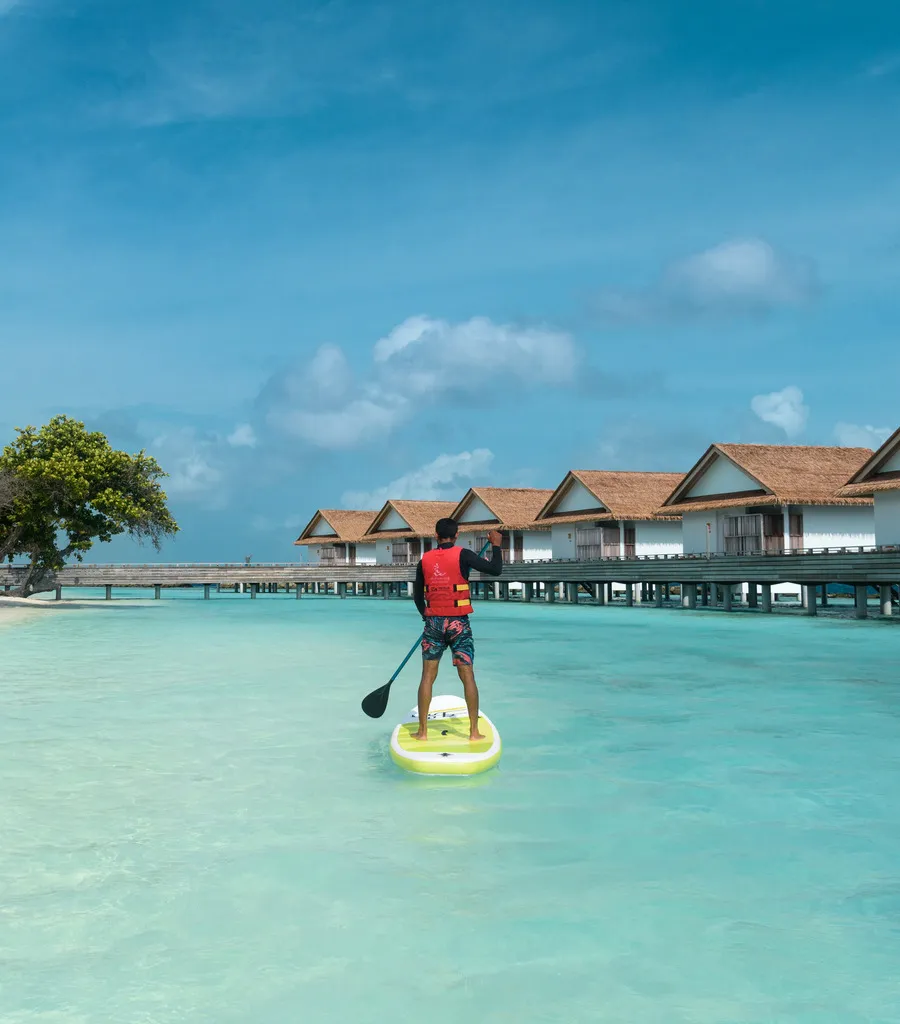 A boy on a paddleboard in the lagoon, the overwater villas behind