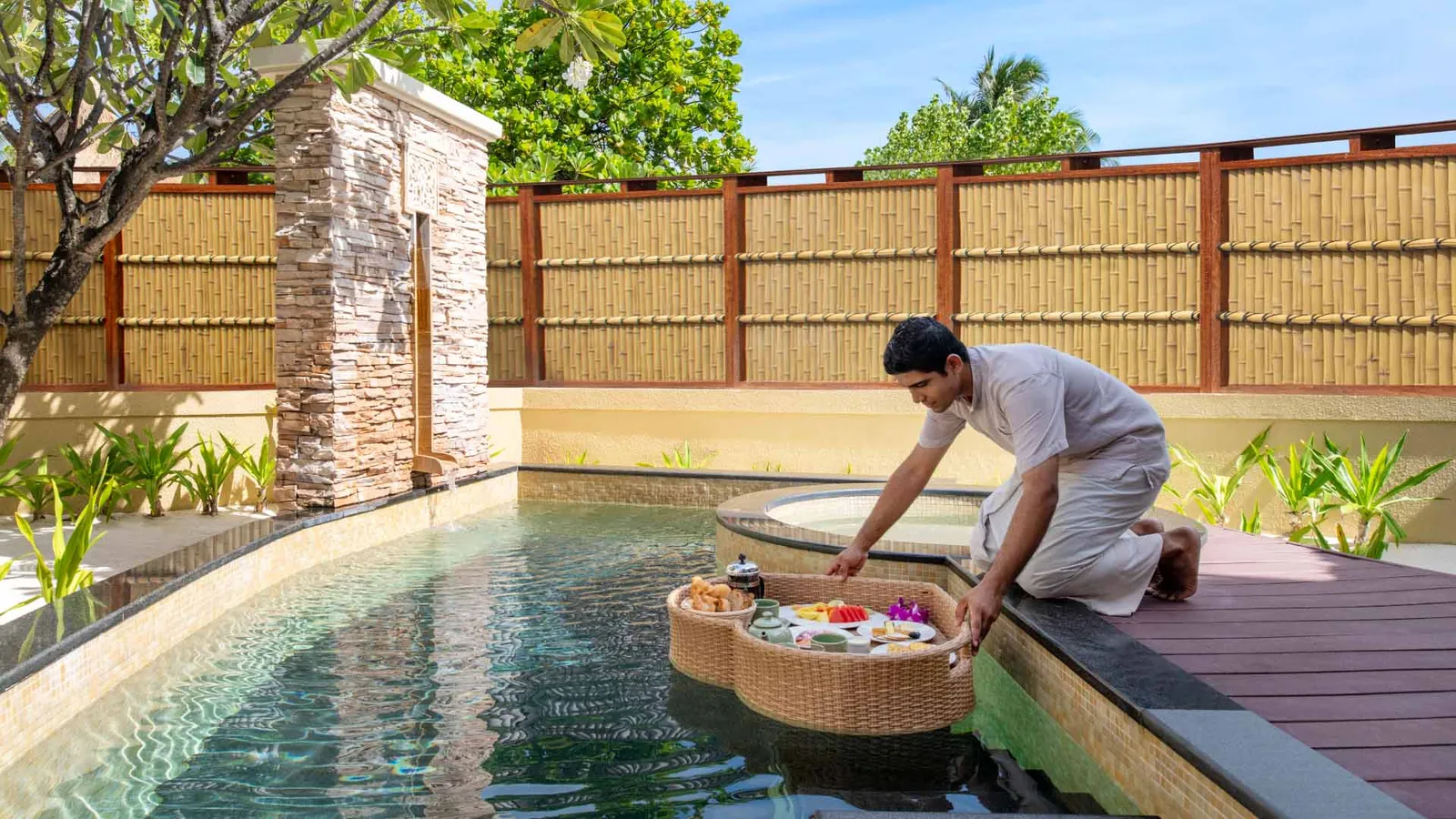 A waiter sets the floating breakfast tray on a villa’s private pool.
