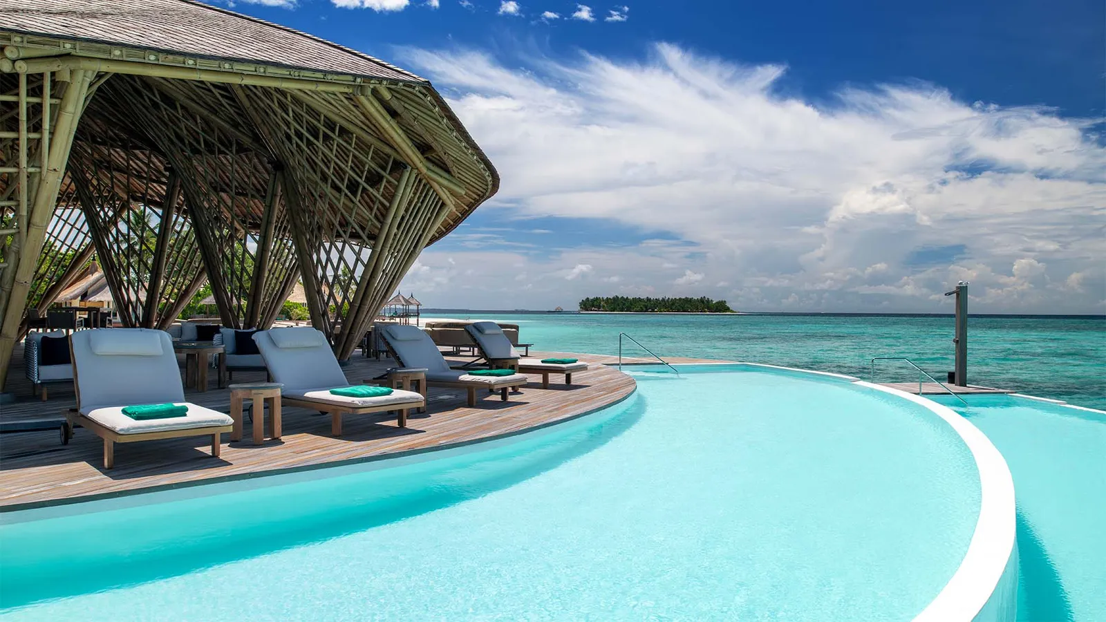 Madi Hiyaa’s saltwater infinity pool, with loungers under the bamboo frame and an island on the horizon.