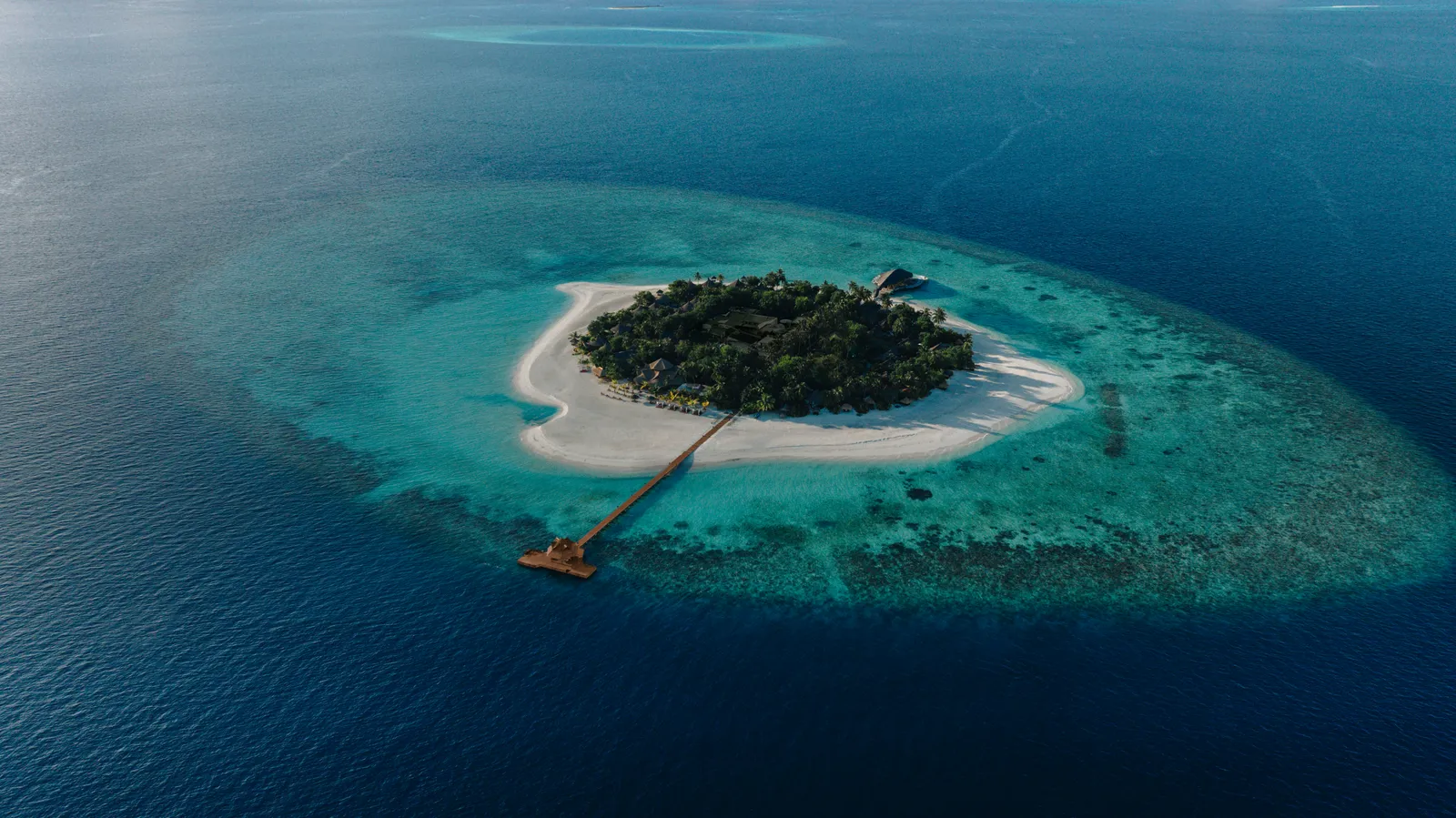 Vabbinfaru seen from afar: a tiny green island, the pale lagoon around it and the jetty pointing out to the blue.