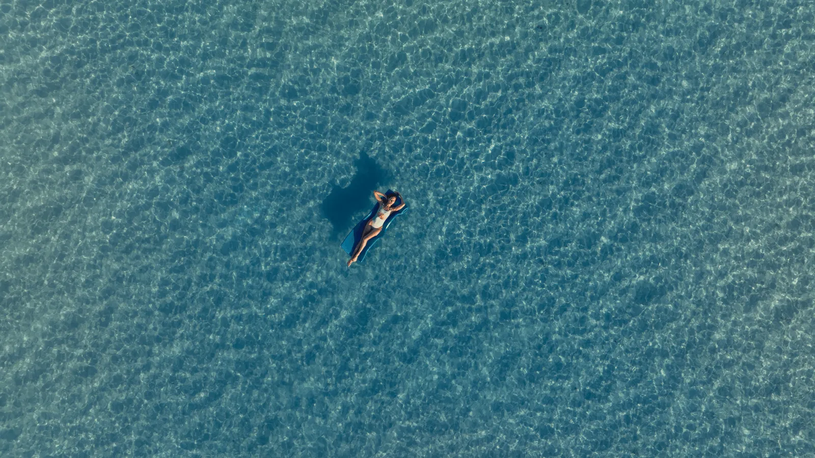 A person floating on their back in the lagoon, seen from above, alone in the clear water.