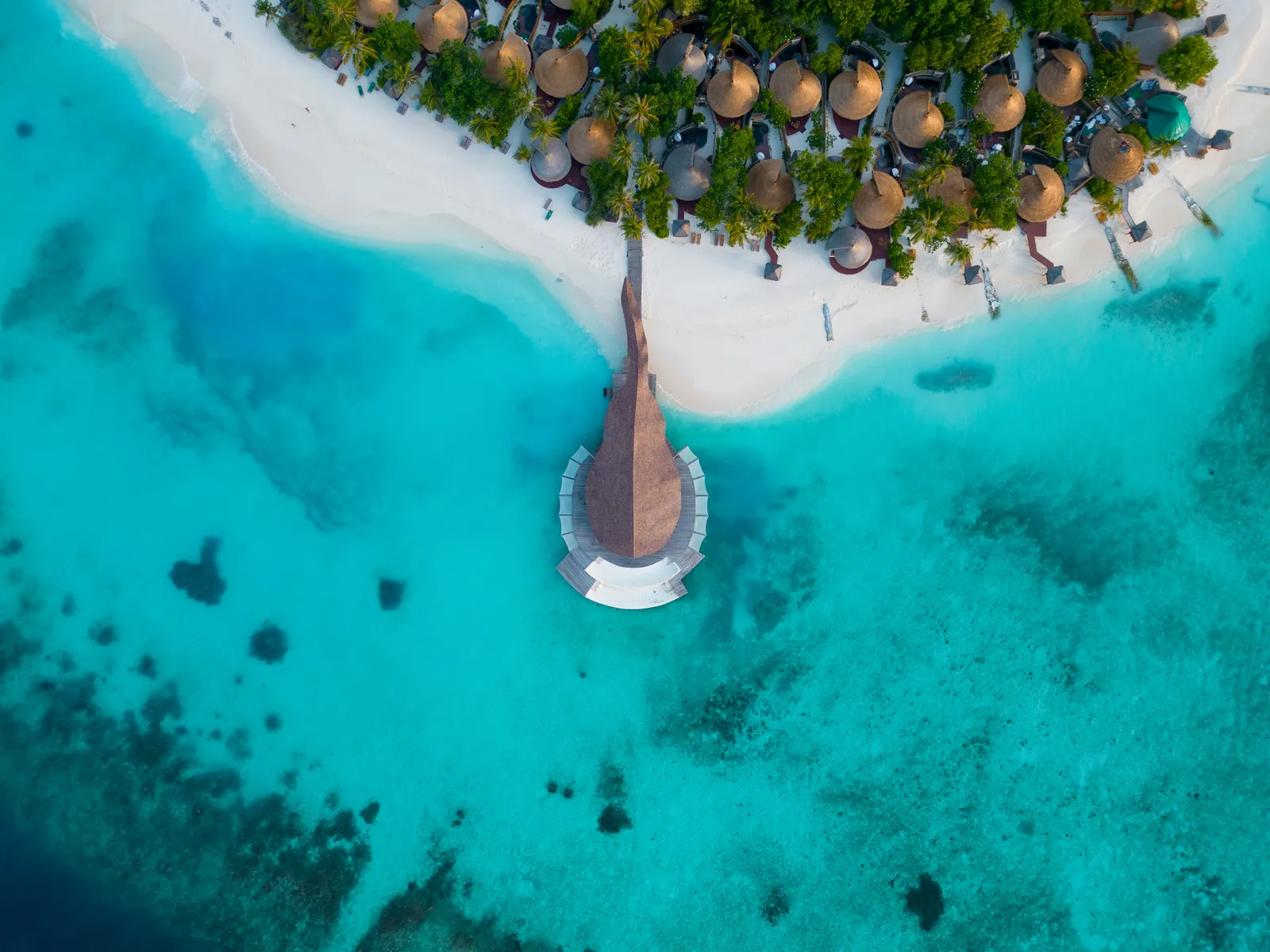 Madi Hiyaa seen straight down: the bamboo roof over the turquoise lagoon, the sandy point and the villas under the palms.