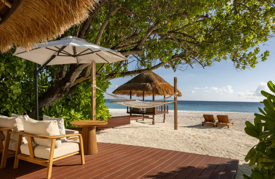 A Beachfront Pool Villa’s deck: armchairs on the timber, the parasol and, a few steps away, the beach and the sala by the sea.