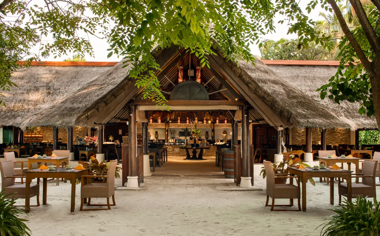 Saffron, the Thai restaurant: the open dining room under thatched roofs, tables laid on the sand among the trees.