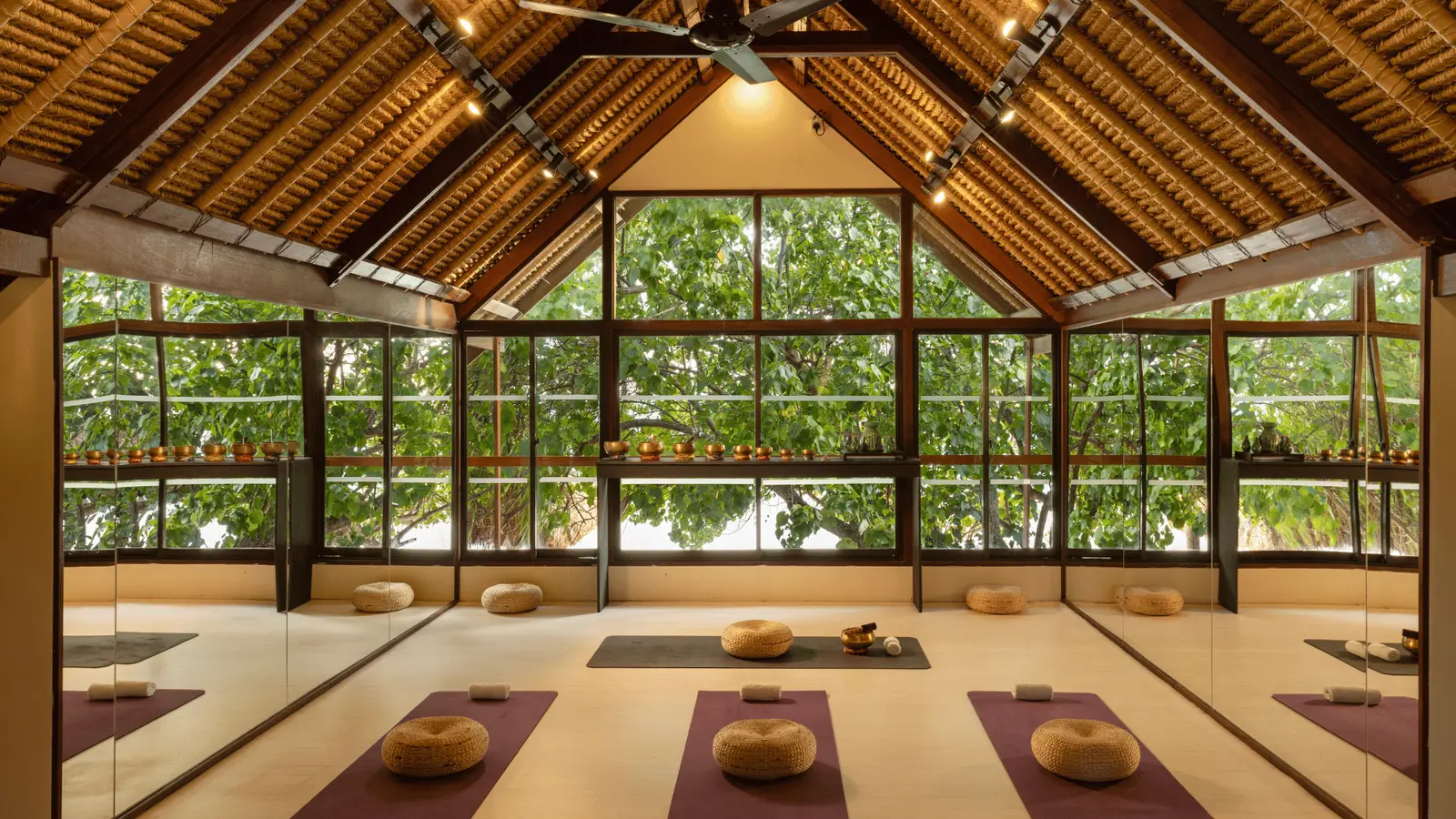 The wellbeing pavilion: mats and cushions on the timber floor, glass walls on the garden under a pitched roof.