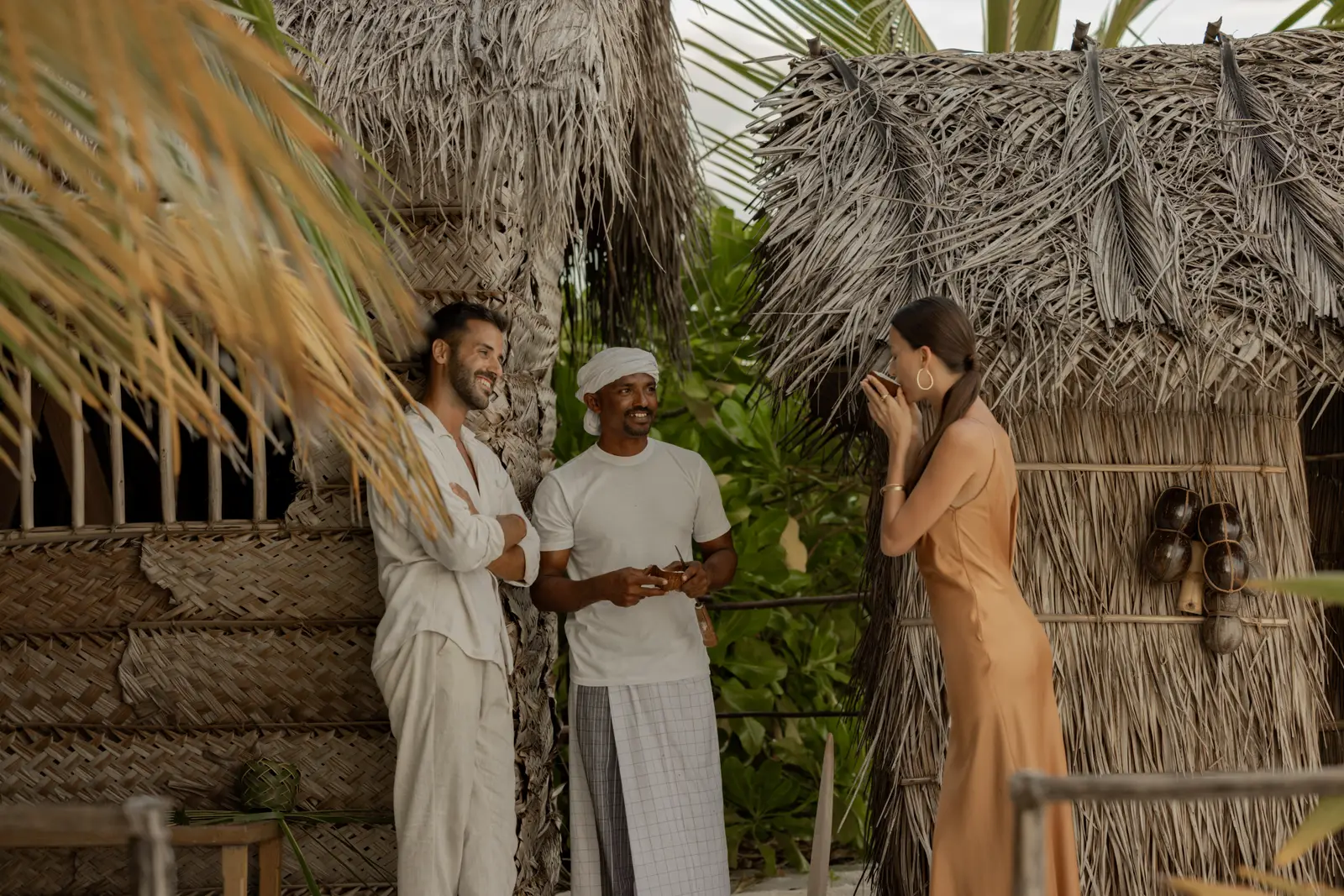 The welcome on arrival: a man in a sarong offers coconut to a couple among the thatched huts.