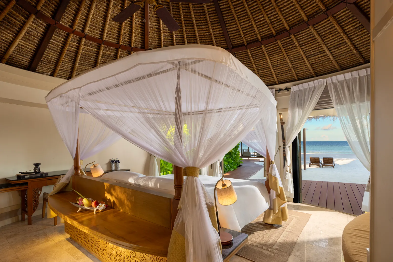 A refreshed villa: the four-poster bed with its cotton mosquito net, the thatched ceiling and the door open to the deck and the sea.