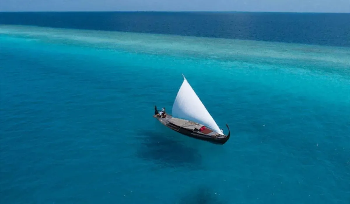 The dhoni Nooma under its white sail on the turquoise lagoon, from above