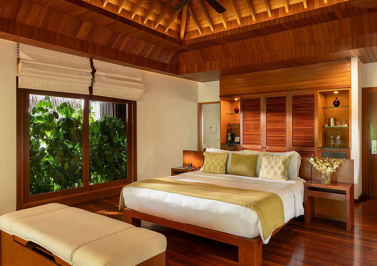 A Baros Villa bedroom, dark wood and windows onto the greenery