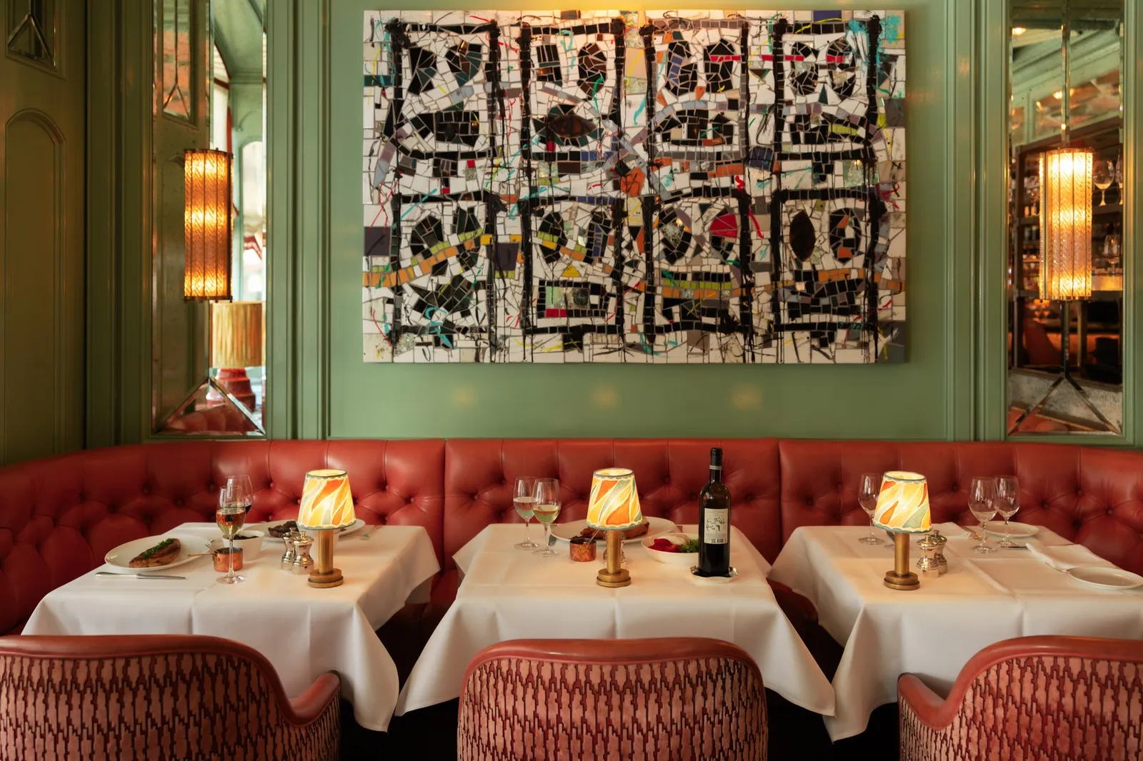 Baur’s Brasserie: red banquettes, laid tables with small lamps, green walls and a large painting by Rashid Johnson