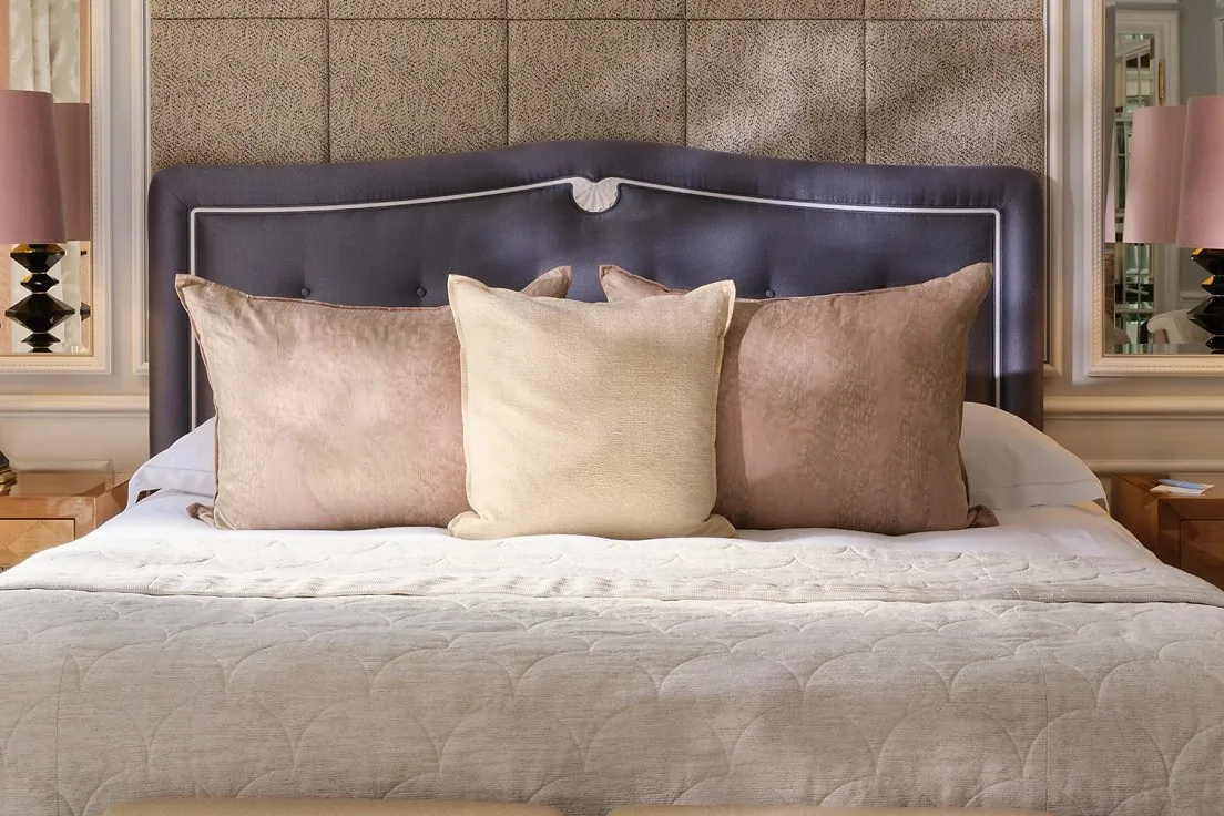 A Junior Suite: a bed with a curved dark headboard, a padded wall behind it and a bench at its foot