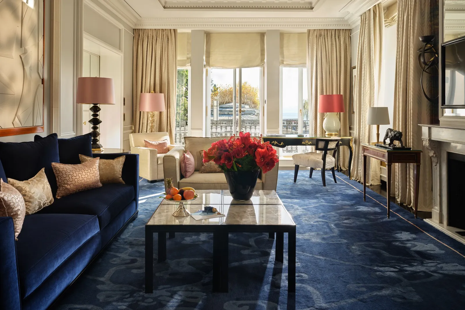The living room of the Lakeside Corner Suite: a navy sofa, red roses on a marble table and tall windows over the park