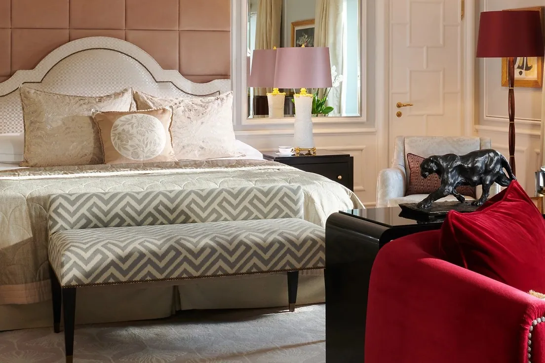 A Lakeside Junior Suite: a bed with a rose headboard, a red velvet armchair and a patterned bench