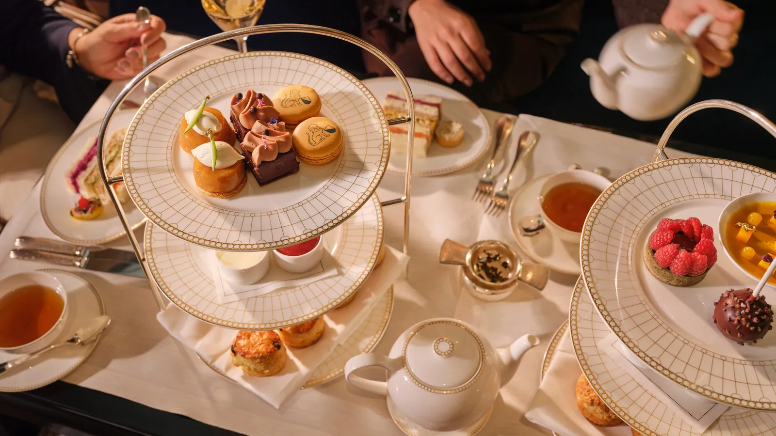 Afternoon tea at Le Hall from above: tiered stands of pastries and scones, teapots and hands reaching for the cups
