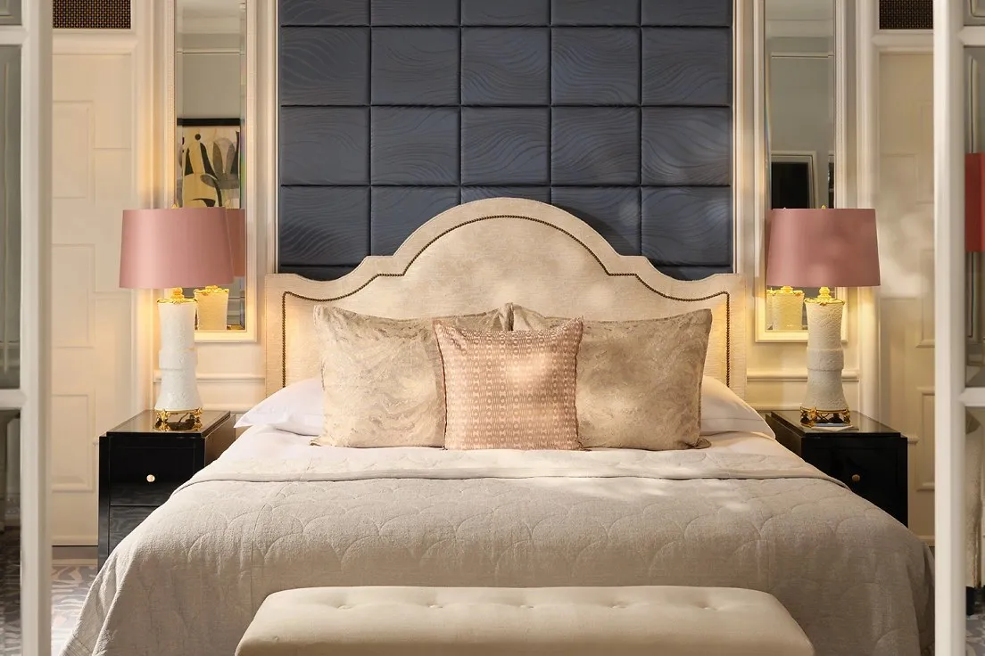 A River Suite: a bed with a curved headboard under a padded navy wall, and pink-shaded lamps