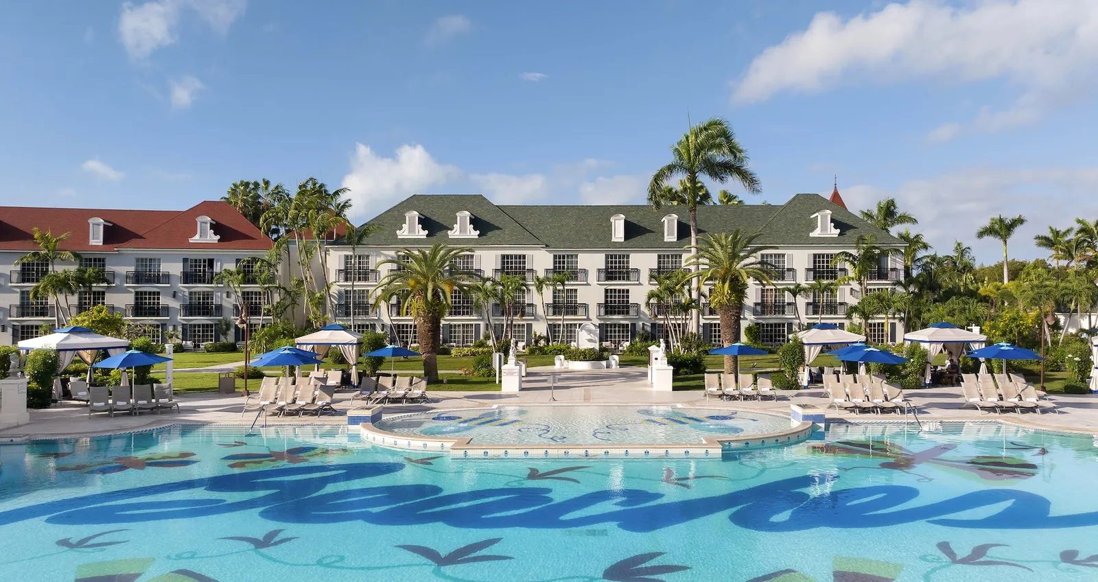 The French Village pool, with the word Beaches on its floor, blue umbrellas and white 3-storey buildings with red roofs.
