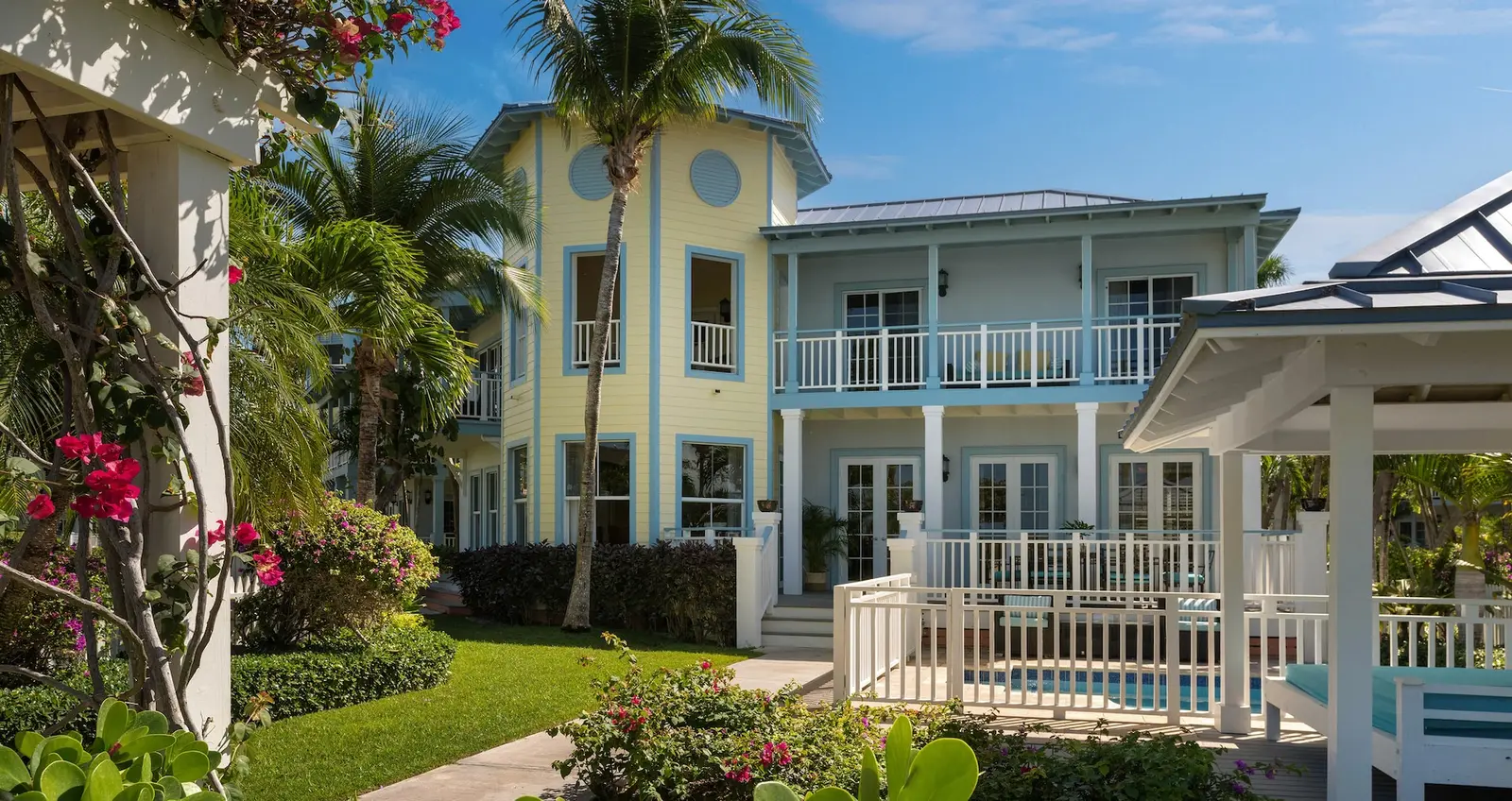 The houses of the Key West Village: yellow and pale blue clapboard fronts with white balconies, a gazebo, a lawn and bougainvillea in flower.
